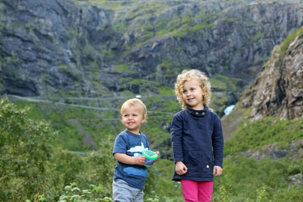 A toddler and a preschooler, from the BabyCanTravel.com family, pose for a picture in Trollstigen, Norway. The toddler is carrying a travel snack cup.