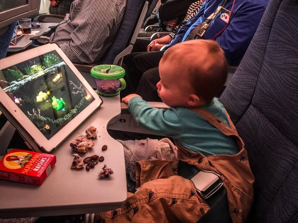 a toddler eats a snack and plays a simple app on an airplane for entertainment.