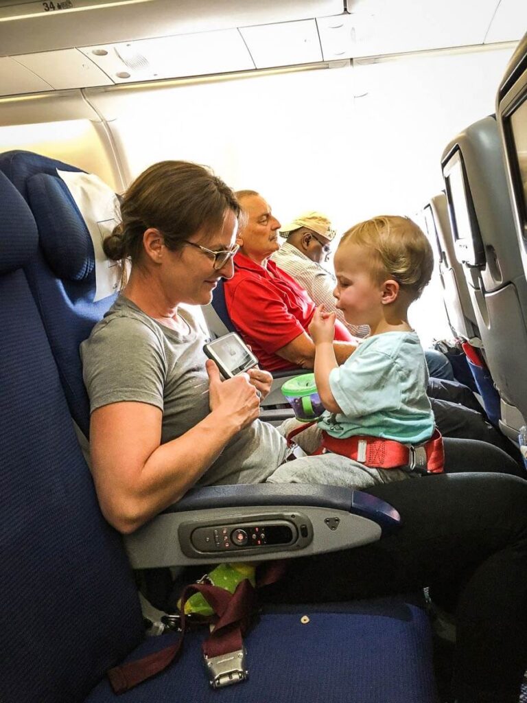 Celine Brewer, owner of BabyCanTravel.com, has her toddler on her lap during a flight and entertains him with a snack and a video on her iPhone.