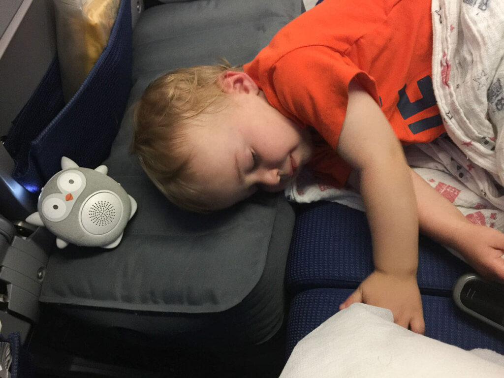 a toddler sleeping on inflatable airplane cushion on airplane.