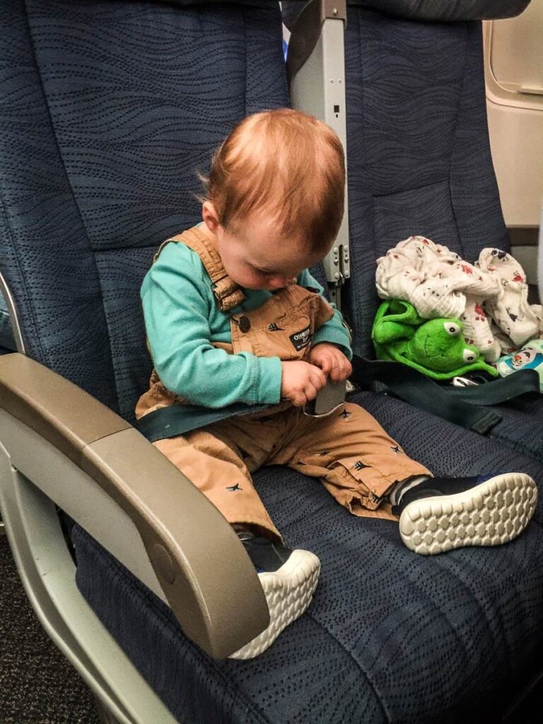 a toddler on airplane playing with his seatbelt.