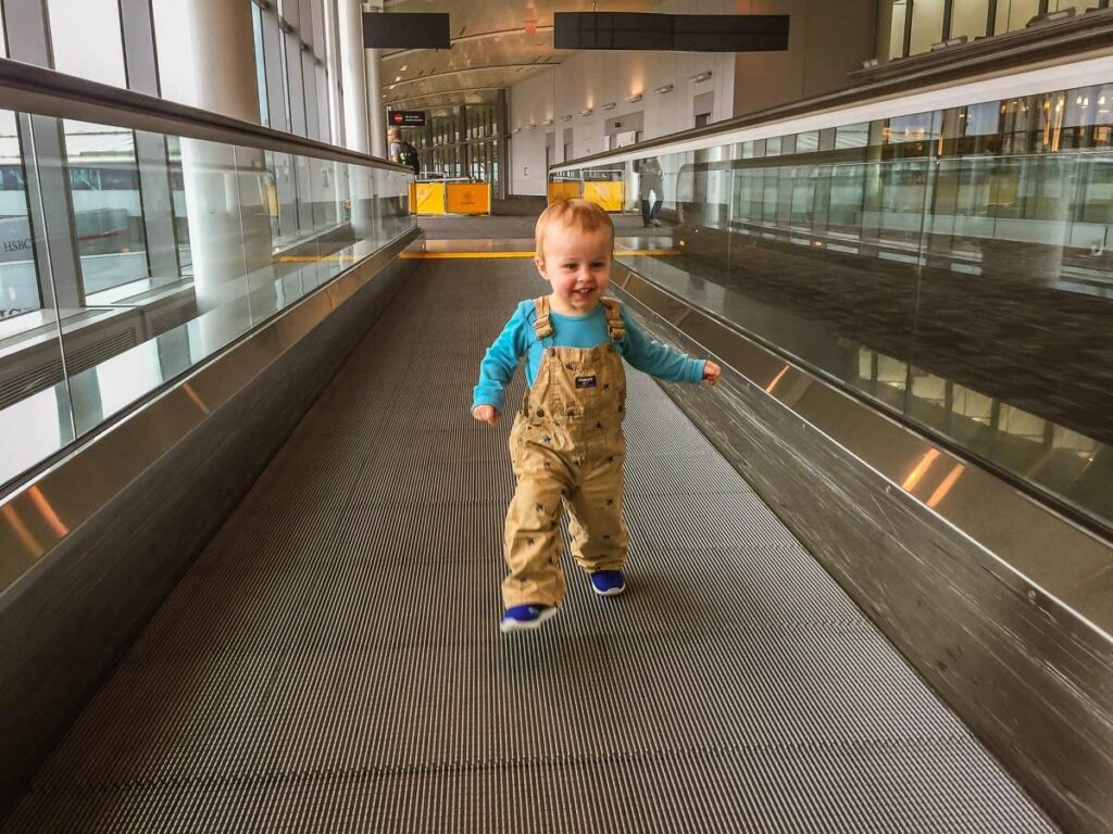 a happy toddler runs in an airport before a family flight.