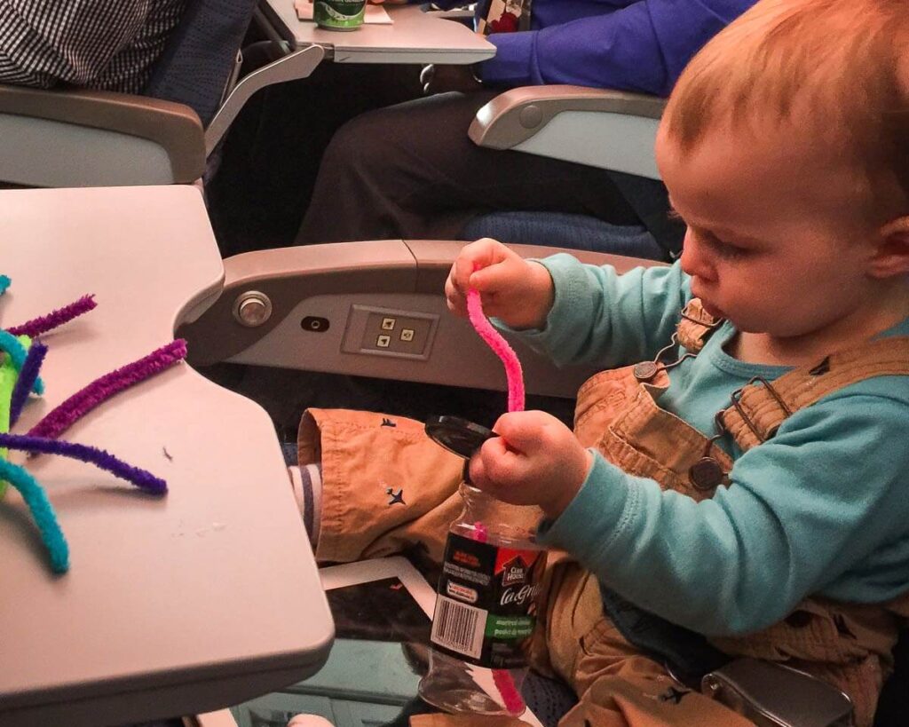 a mother entertains her toddler on a flight with a homemade toy made of pipe cleaners and spice jars.