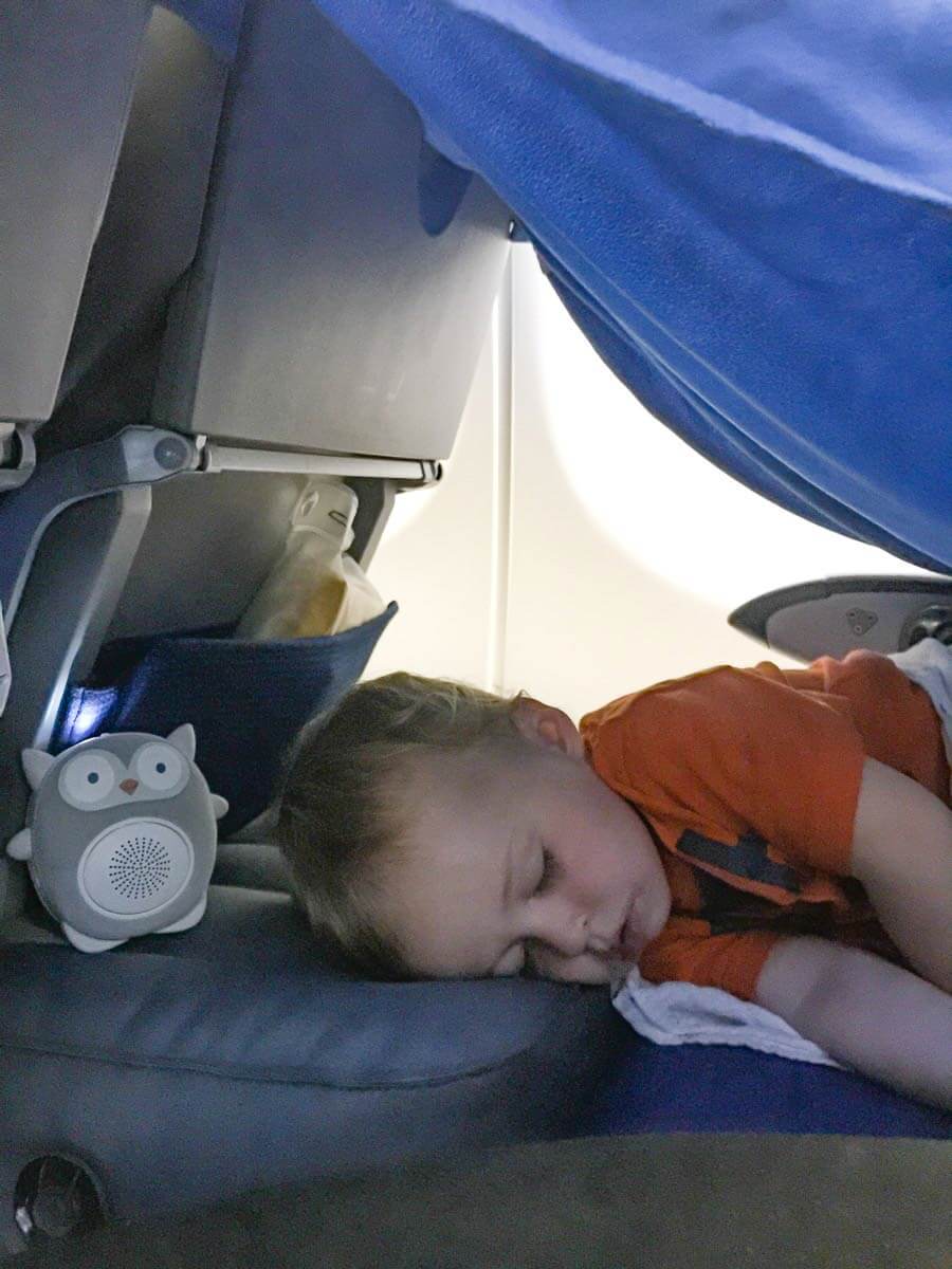 a 2 year old, from the BabyCanTravel.com family, sleeps soundly on a toddler airplane bed during a long haul flight with his family.