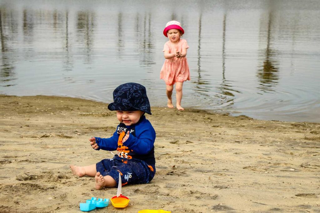 A baby and toddler on vacation in San Diego play on the beach near Mission Beach