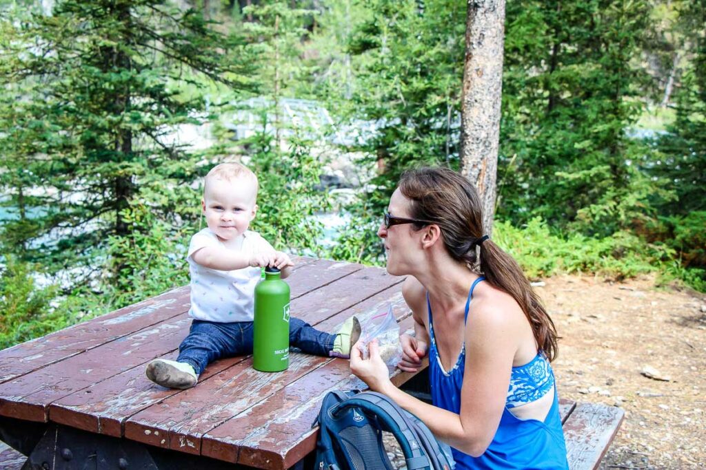 a baby sits on a picnic table while hiking with her mom