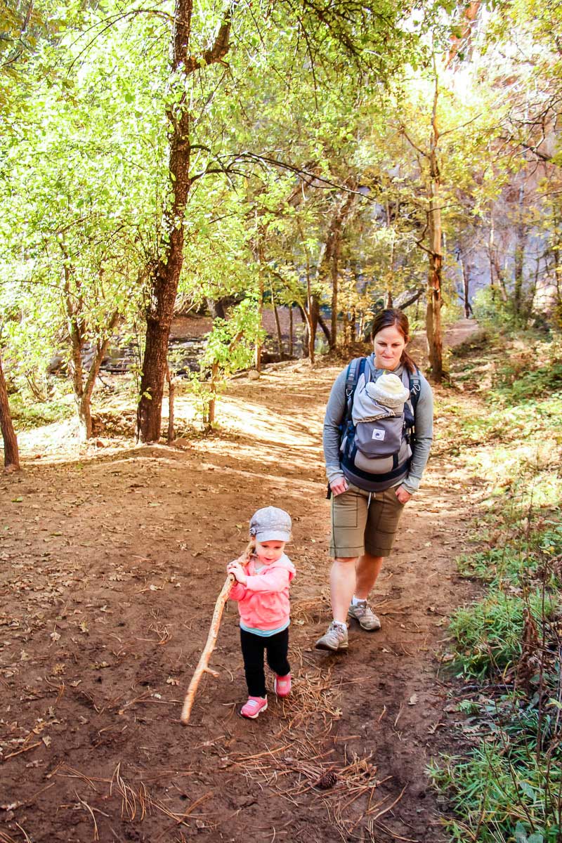 a Mom carries her baby on her front, while she goes hiking with her toddler in Sedona, AZ.