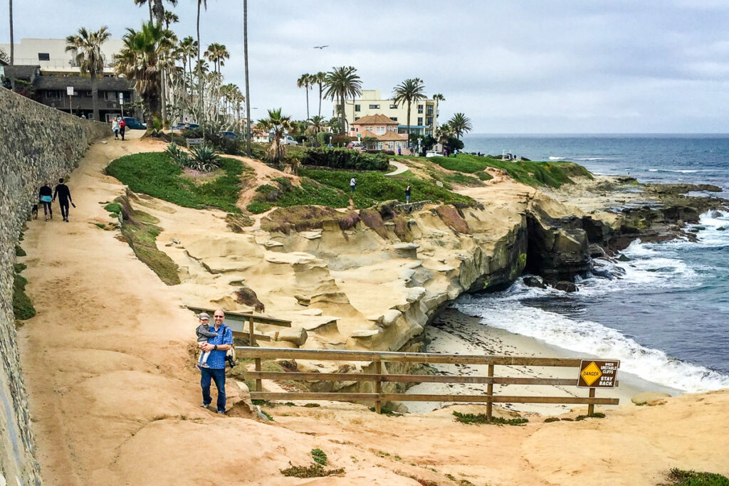 A Dad holds his toddler along the coastline in La Jolla, San Diego - a great place for an easy family walk.