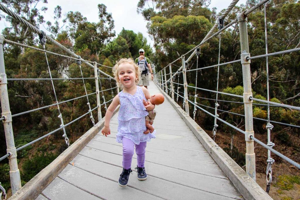 A toddler holding a doll runs across the Spruce Street Suspension Bridge near Balboa Park, San Diego.