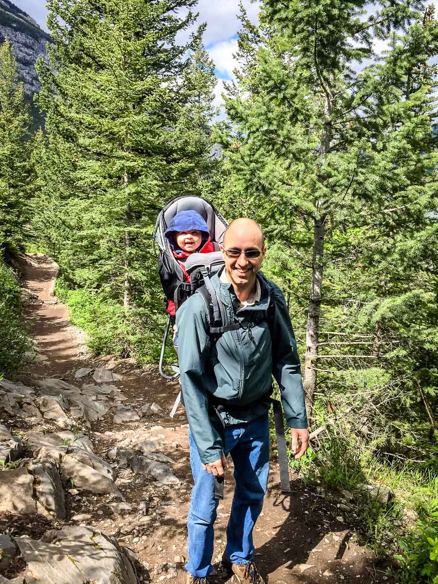 A Dad carries his toddler in a Deuter Kid Comfort backpack carrier while on a family hike. 