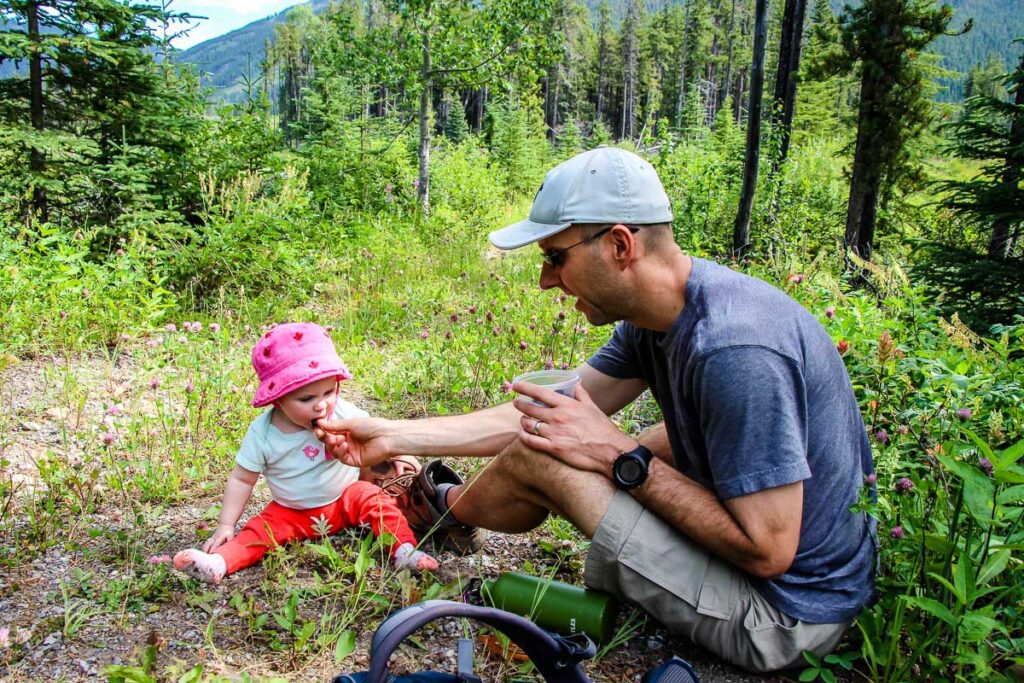 a dad feeding baby while hiking