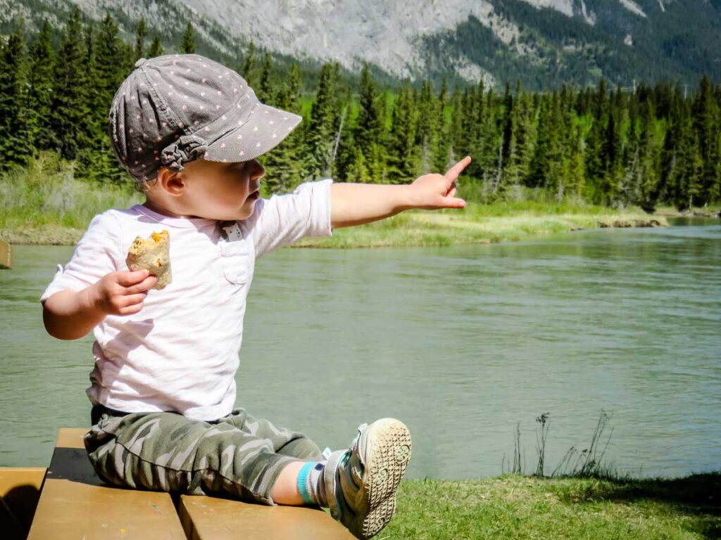 A family hiking with a toddler stops by a river for a snack.