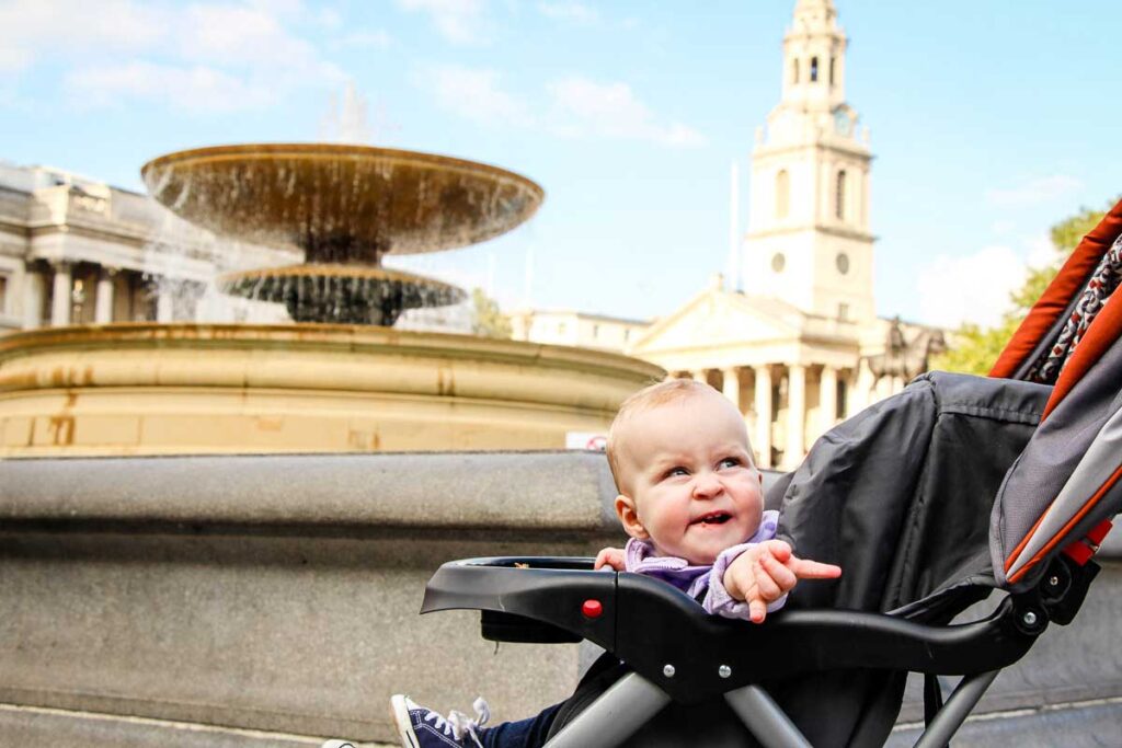 baby in stroller in front of fountain in Trafalgar Square London