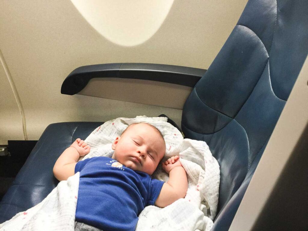 a baby sleeps soundly over two seats on a family flight.