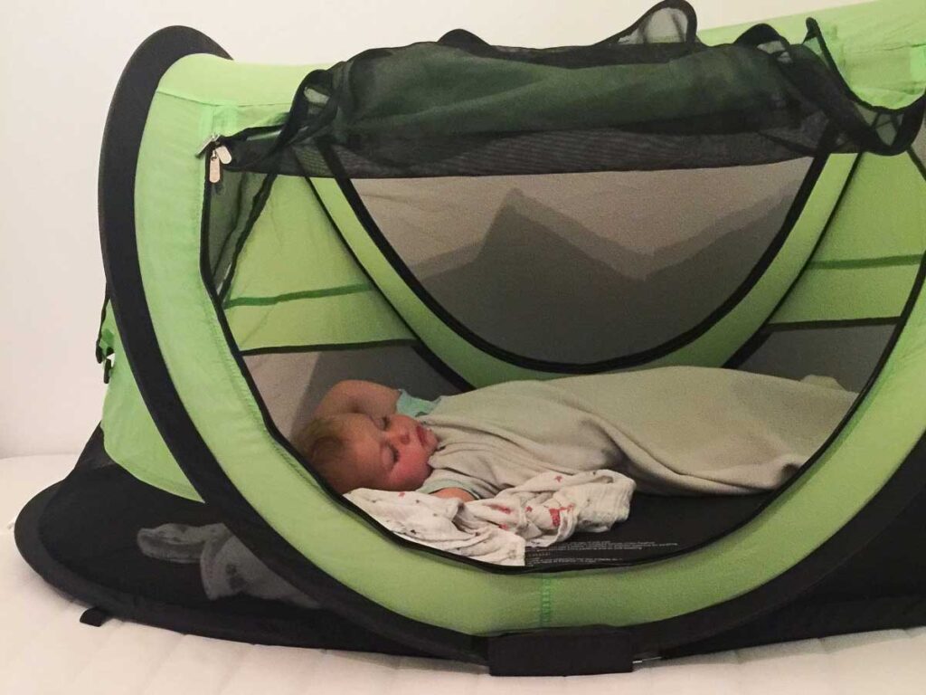 a baby sleeps in a KidCo PeaPod Plus Toddler Travel bed while on a family trip in Japan.