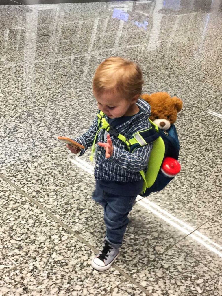 a toddler wears a backpack carrying some toys and his favorite stuffy - a great strategy for flying with a toddler.