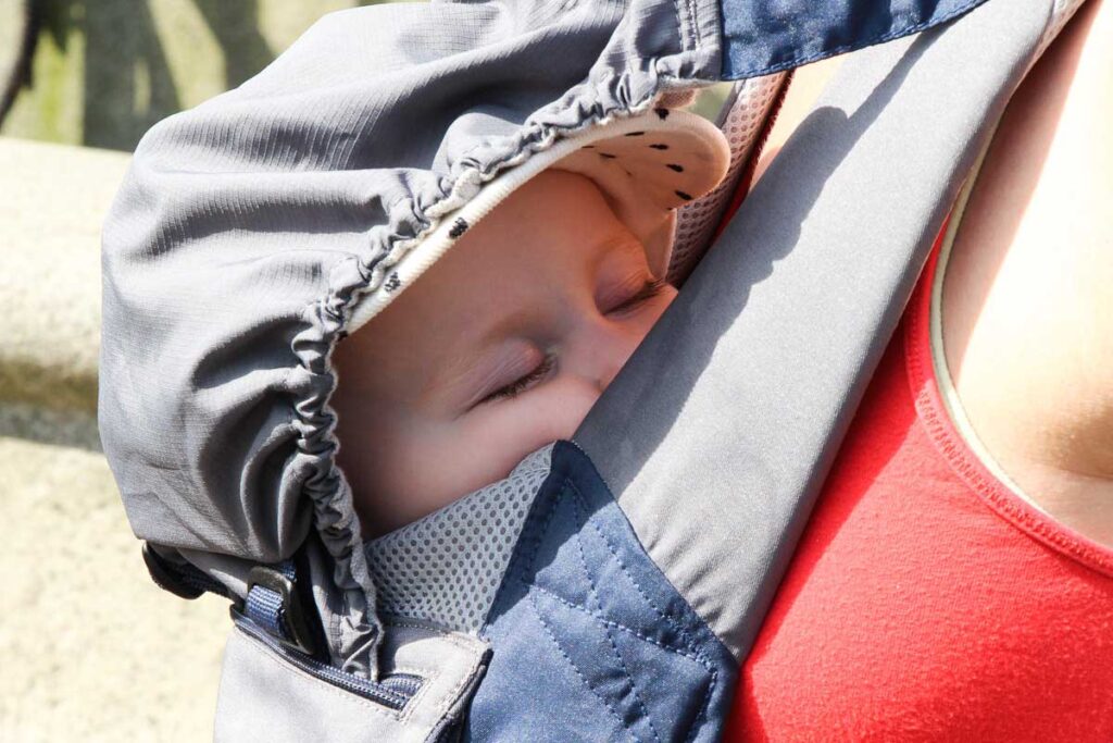 baby sleeping in baby carrier - one of the must-have baby travel gear items