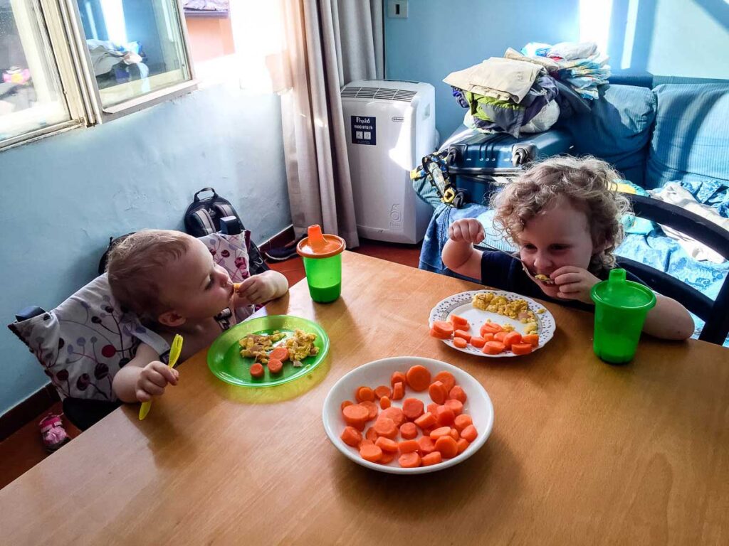 The BabyCanTravel.com kids eat a meal on a family vacation to Italy. The toddler is contained in a travel high chair, while the preschooler is trusted to sit nicely on her own.