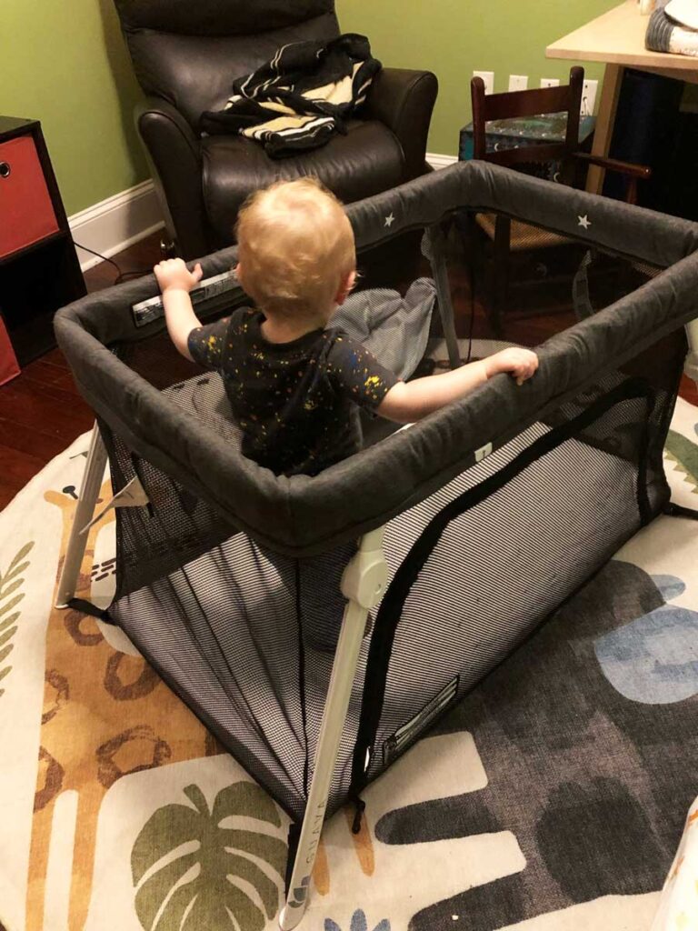 a baby stands in a Guava Lotus Travel Crib in an Airbnb