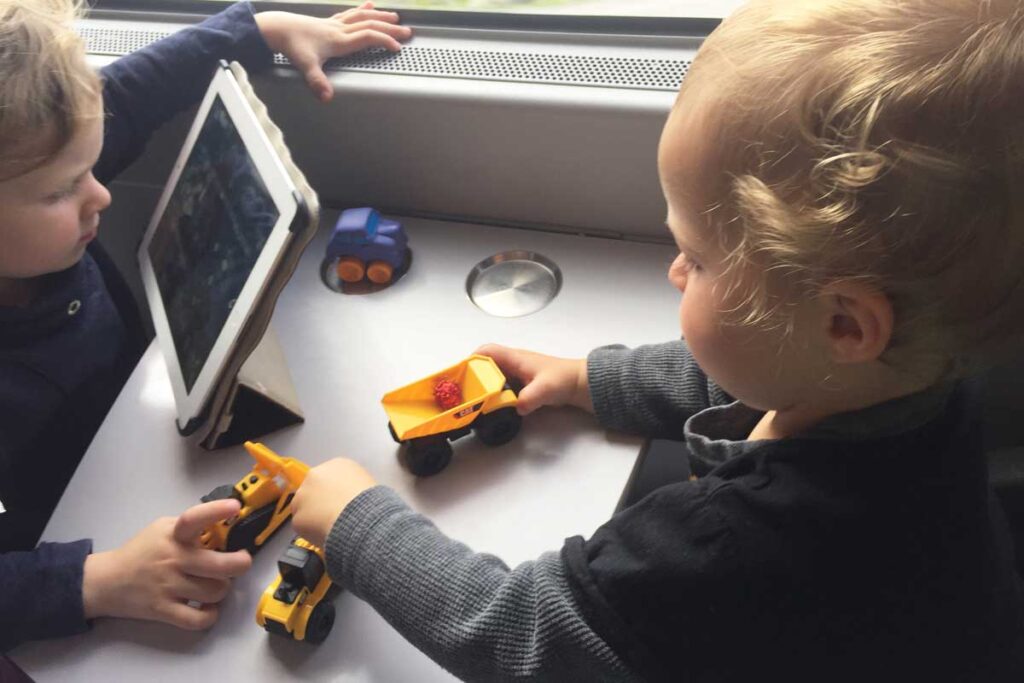 two toddlers from BabyCanTravel.com play with pom poms and construction trucks on a train trip during a family vacation.