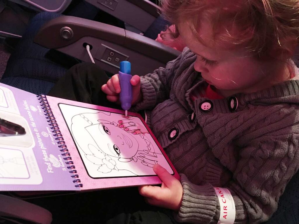 a toddler from the BabyCanTravel.com family plays with a screen-free Water Wow coloring book while on an airplane during a family vacation.