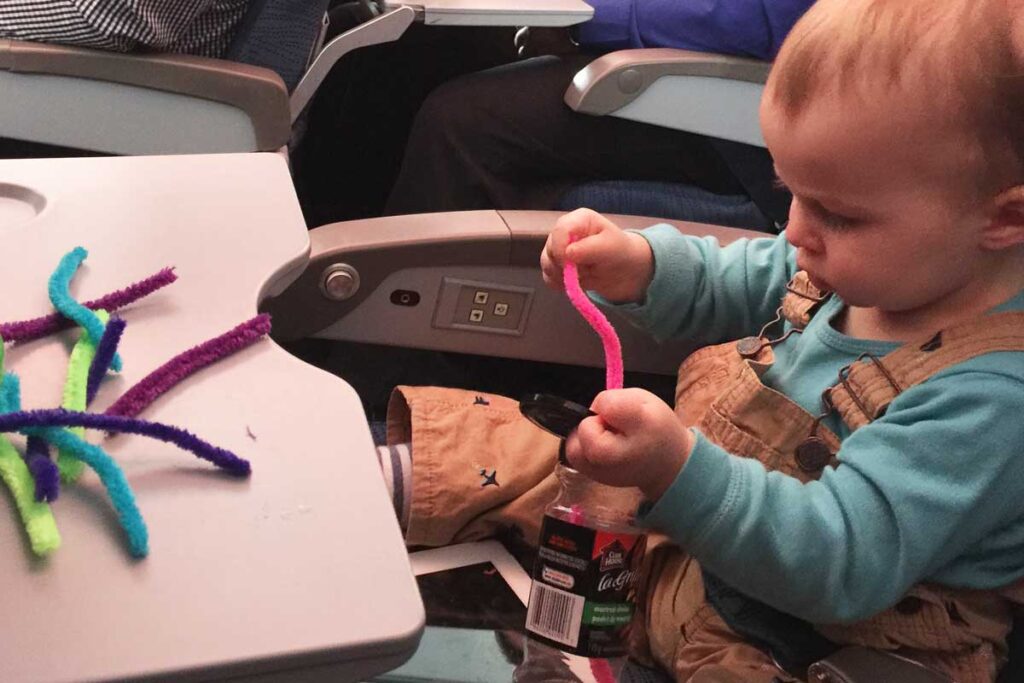 a toddler from BabyCanTravel.com, plays with a DIY toddler travel toy on a plane during a family vacation.