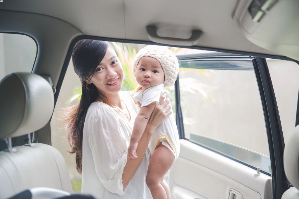 A mother places her baby into a car seat in the car