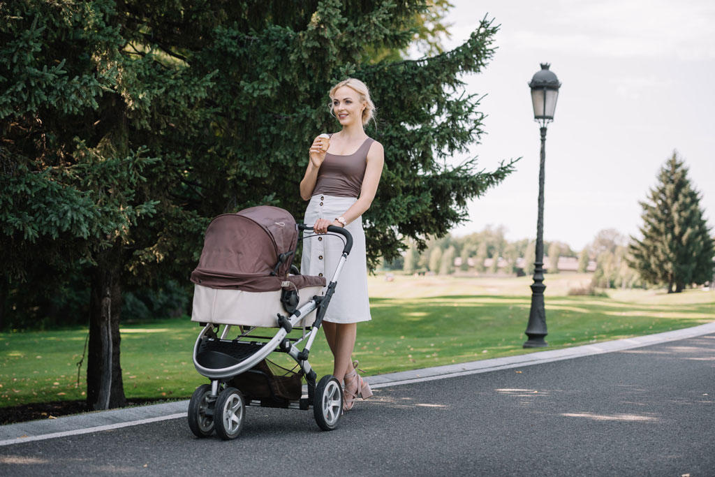 a mother pushes a travel stroller for infant with carrycot.