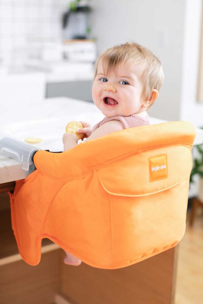 a baby eats a cracker while sitting in an Inglesina Fast Table Chair - a portable high chair for travel with baby.