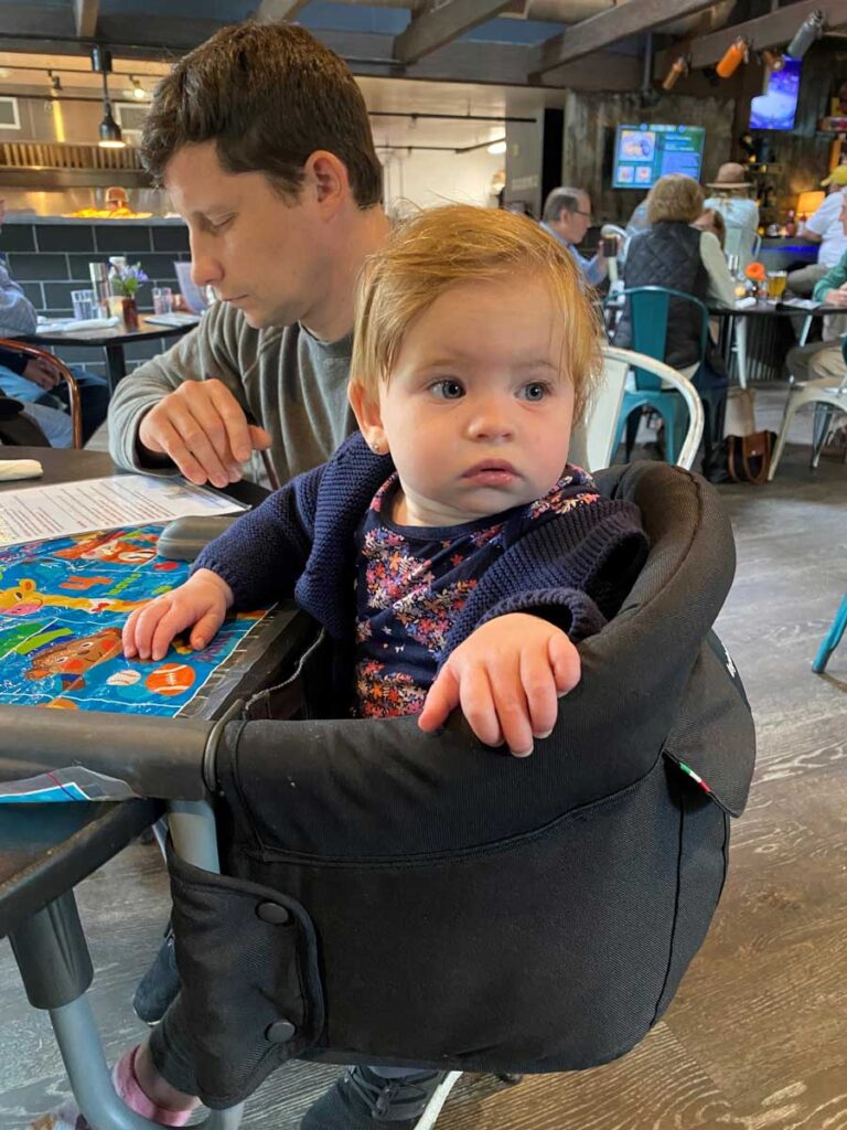 a baby sitting in Inglesina high chair attached to a table at a restaurant.