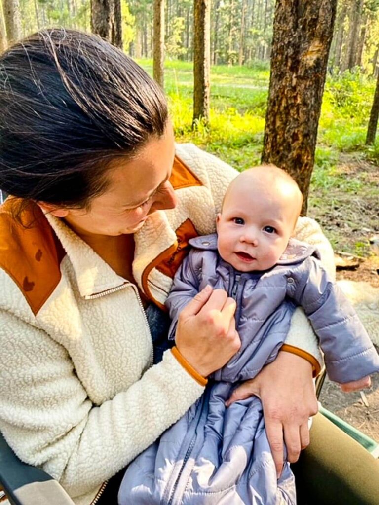 a mother holds her baby who is wearing a camping sleeping bag for baby.