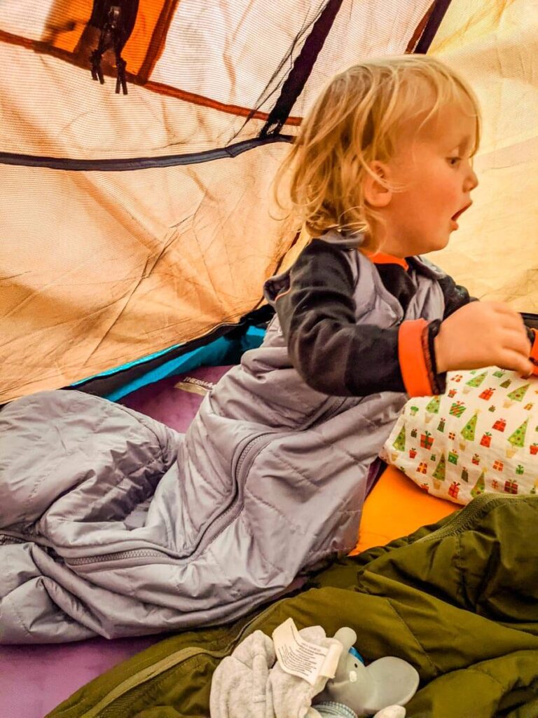 toddler crawling in tent wearing toddler sleeping bag for camping.