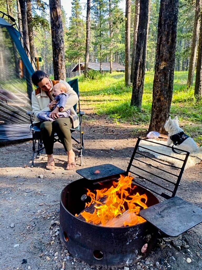 a mother holds her baby who is wearing the Baby Deedee Sleep Nest Travel while camping with her family.