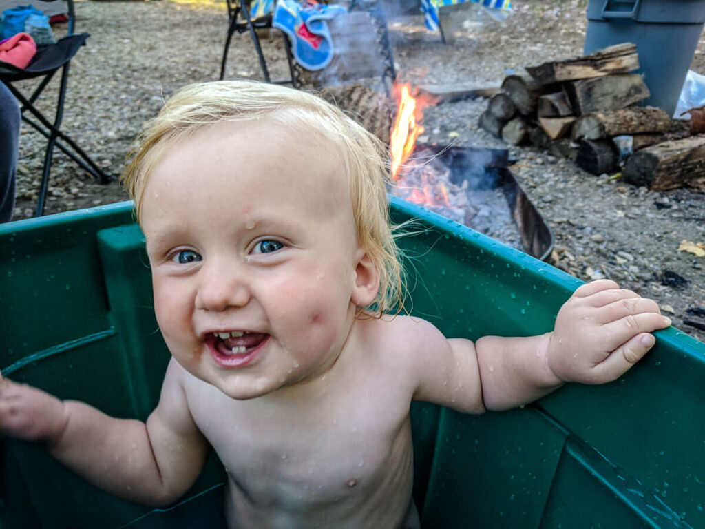 a toddler enjoys an outdoor bath near the campfire while on a family camping adventure.