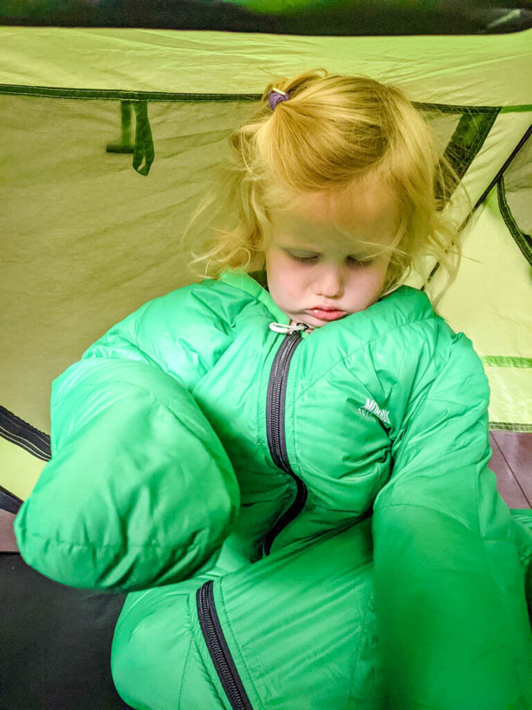 toddler wearing a Morrison Outdoors toddler sleeping bag in Peapod Plus toddler bed for camping.