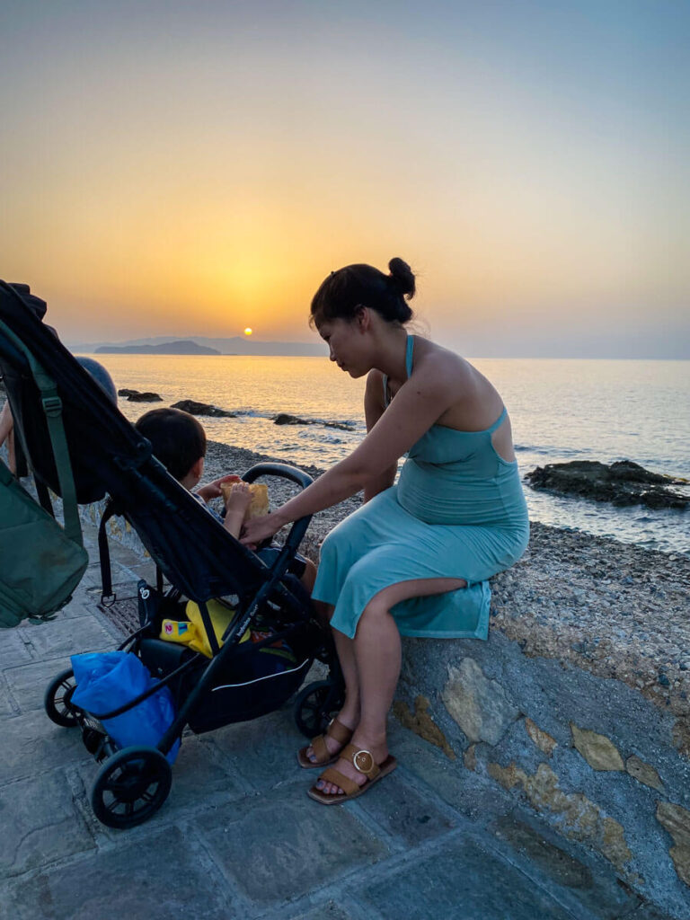 mother tending to toddler in a foldable compact stroller at sunset by the beach.