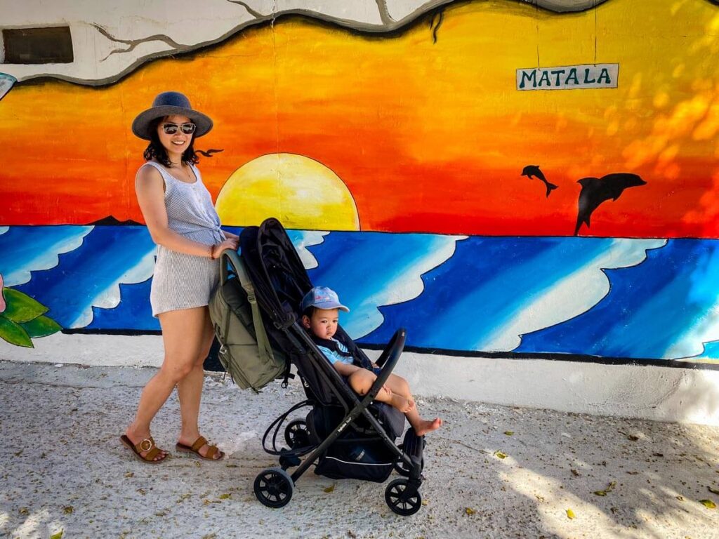 a mom pushes a lightweight stroller while on a family vacation with her toddler.