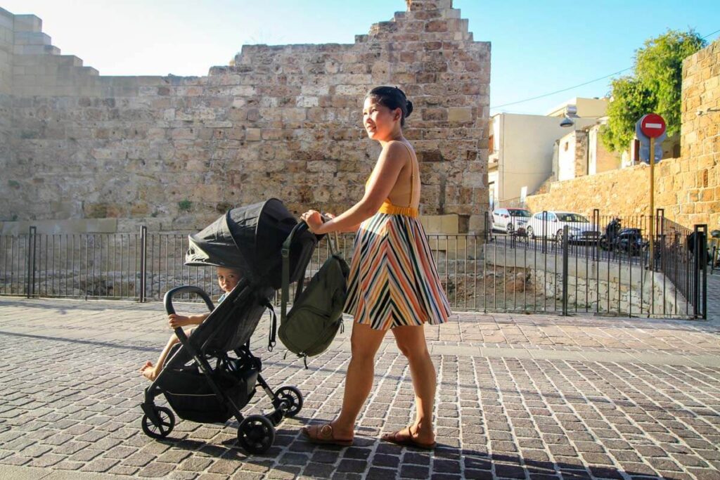 Mother pushing foldable compact stroller in Greece with the large sun shade pulled down.