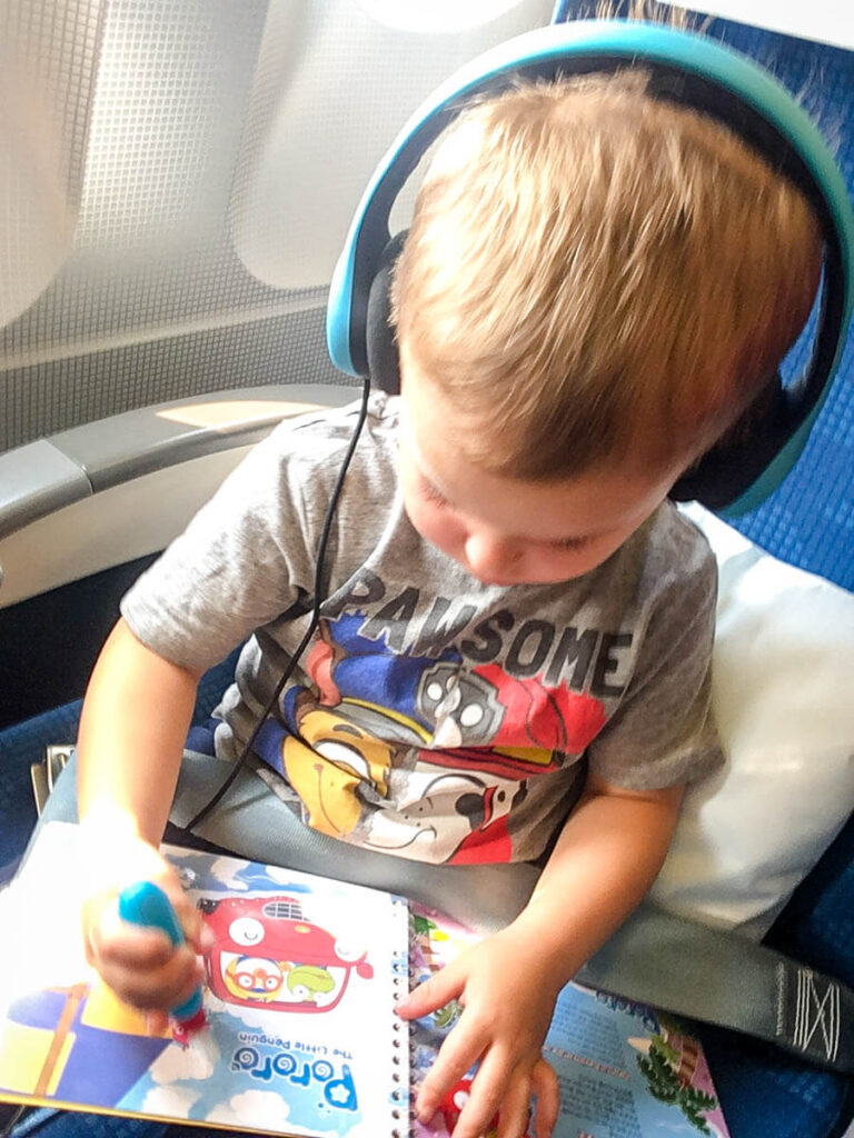 toddler on plane wearing airplane safe headphones.