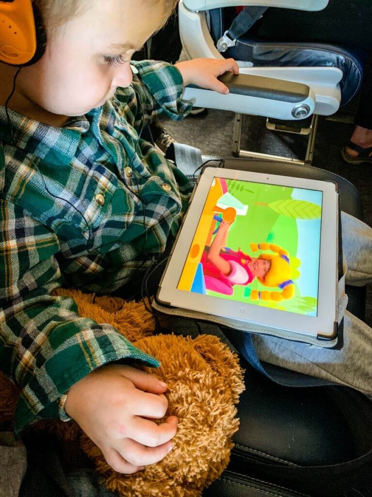 a toddler watching ipad while wearing toddler airplane headphones.