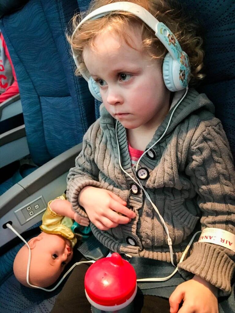 toddler on airplane wearing toddler safe headphones.