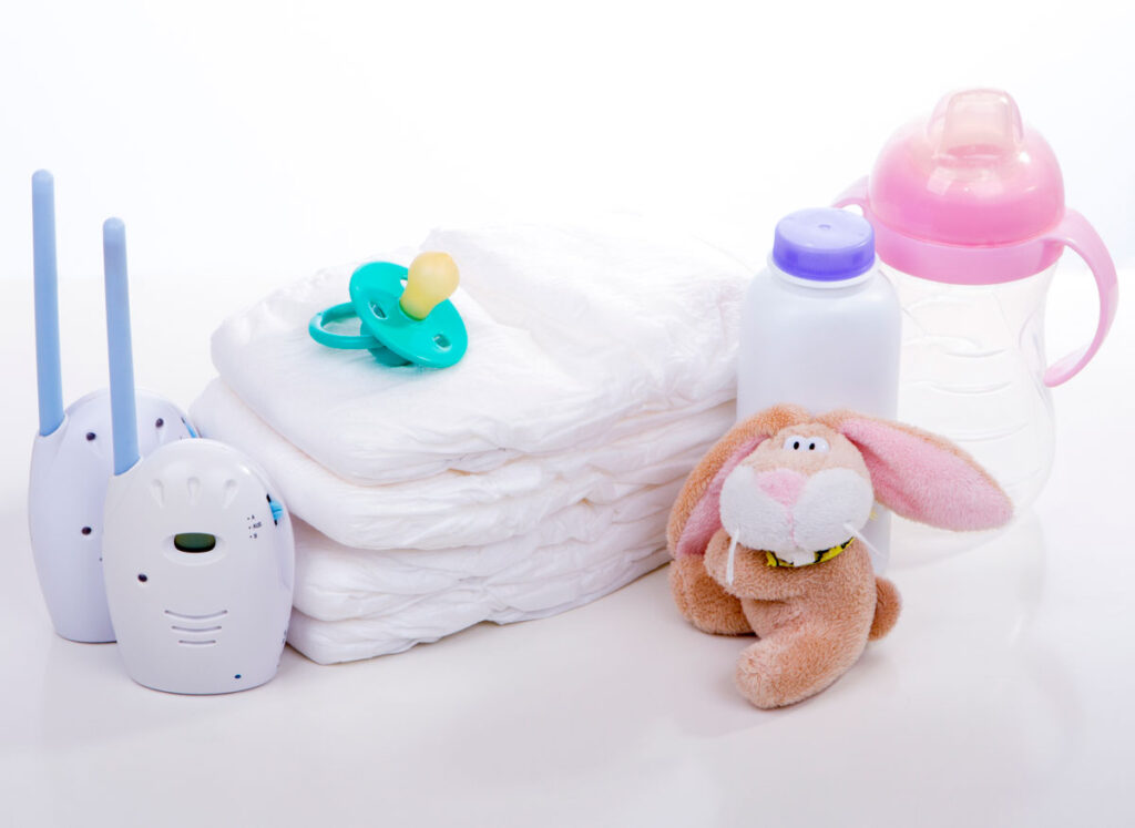 baby monitor beside a pile of diapers, stuffy and bottles.