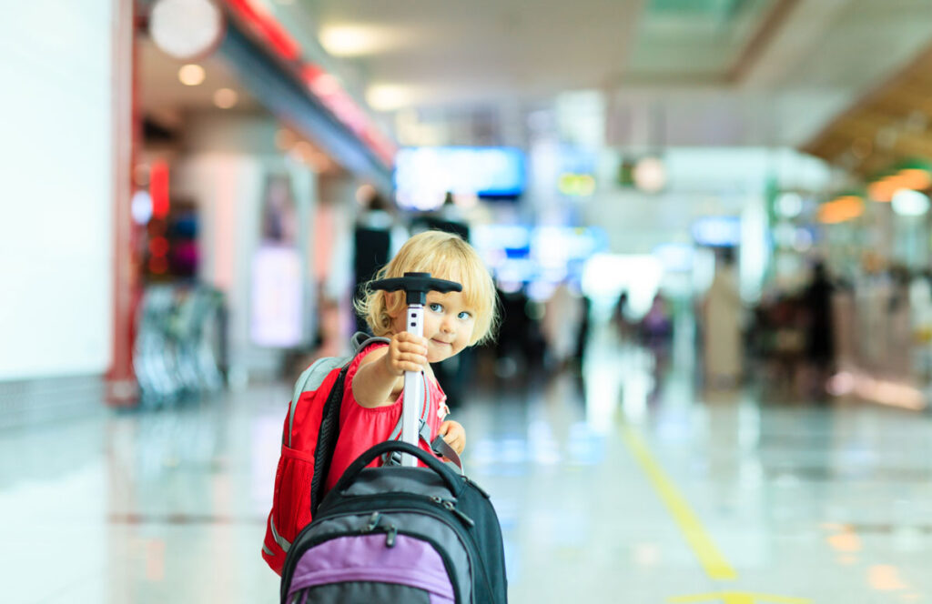 toddler in airport holding handle of suitcase for toddlers.