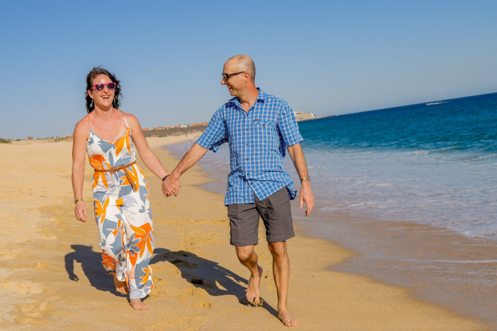 Two parents without kids hold hands on the beach at a family-friendly all-inclusive resort in Cabo San Lucas Mexico.