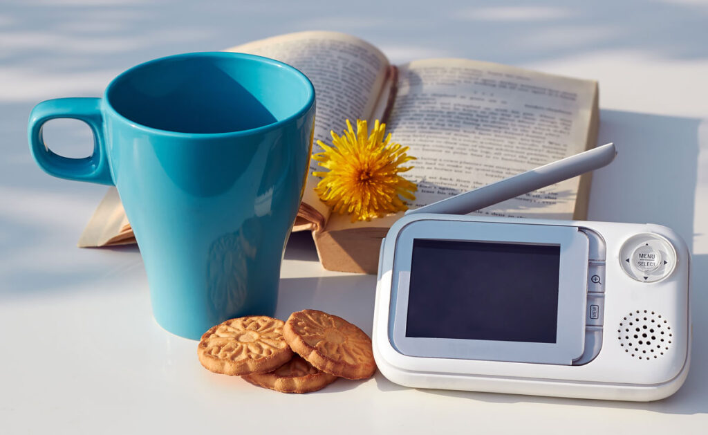 travel baby monitor on table with coffee mug, cookies and book.