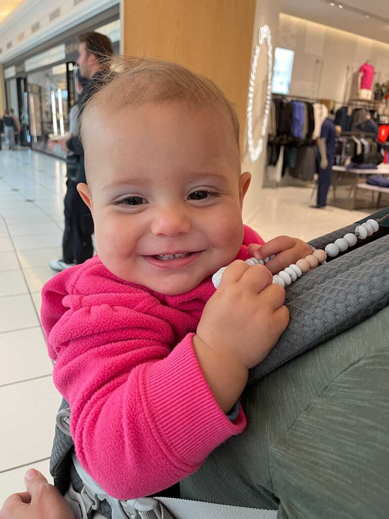 baby in carrier playing with teething necklace.