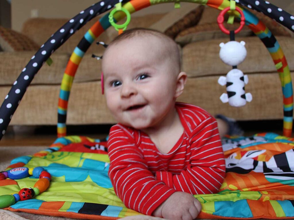 a baby from BabyanTravel.com is all smiles while playing on a portable baby travel play mat.