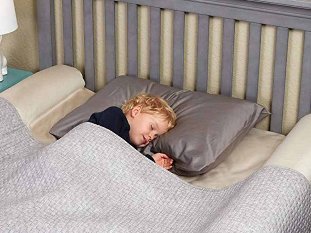 child sleeping on a hotel bed with hiccapop inflatable bed rails positioned on each side under sheets