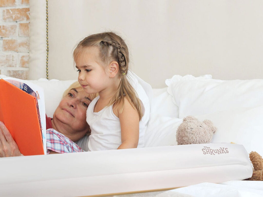 grandmother and child on a hotel bed next to a shrunks inflatable bed rail for toddlers