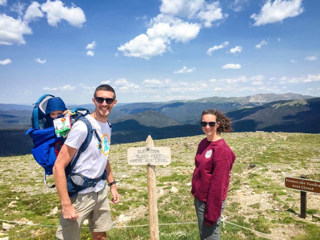 parents near elevation sigh while hiking Ute Trail in Rocky Mountain National Park with a Baby